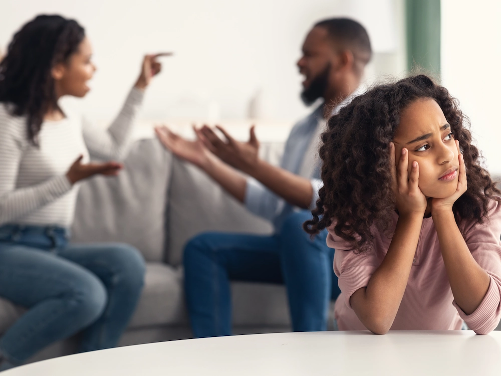Photo showing parents sitting on the couch in a verbal argument with young girl in the foreground