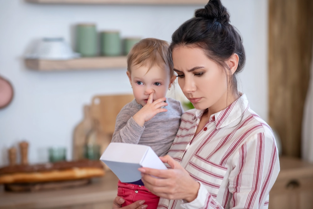 Single mother holding young child while reading package label